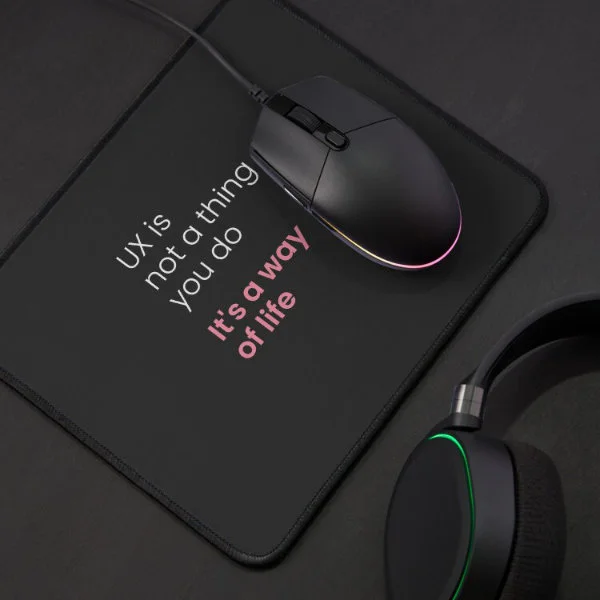 A mouse pad with the phrase "UX is not a thing you do, it&rsquo;s a way of life" in white and pink letters.