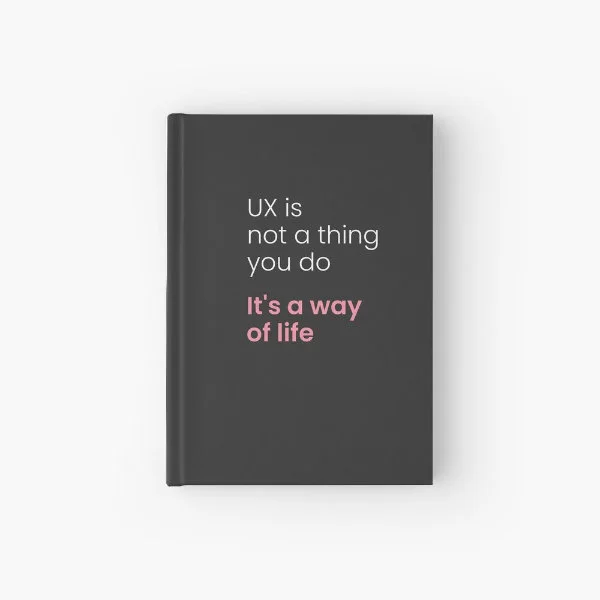 A hardcover journal with the phrase "UX is not a thing you do, it&rsquo;s a way of life" in white and pink letters.